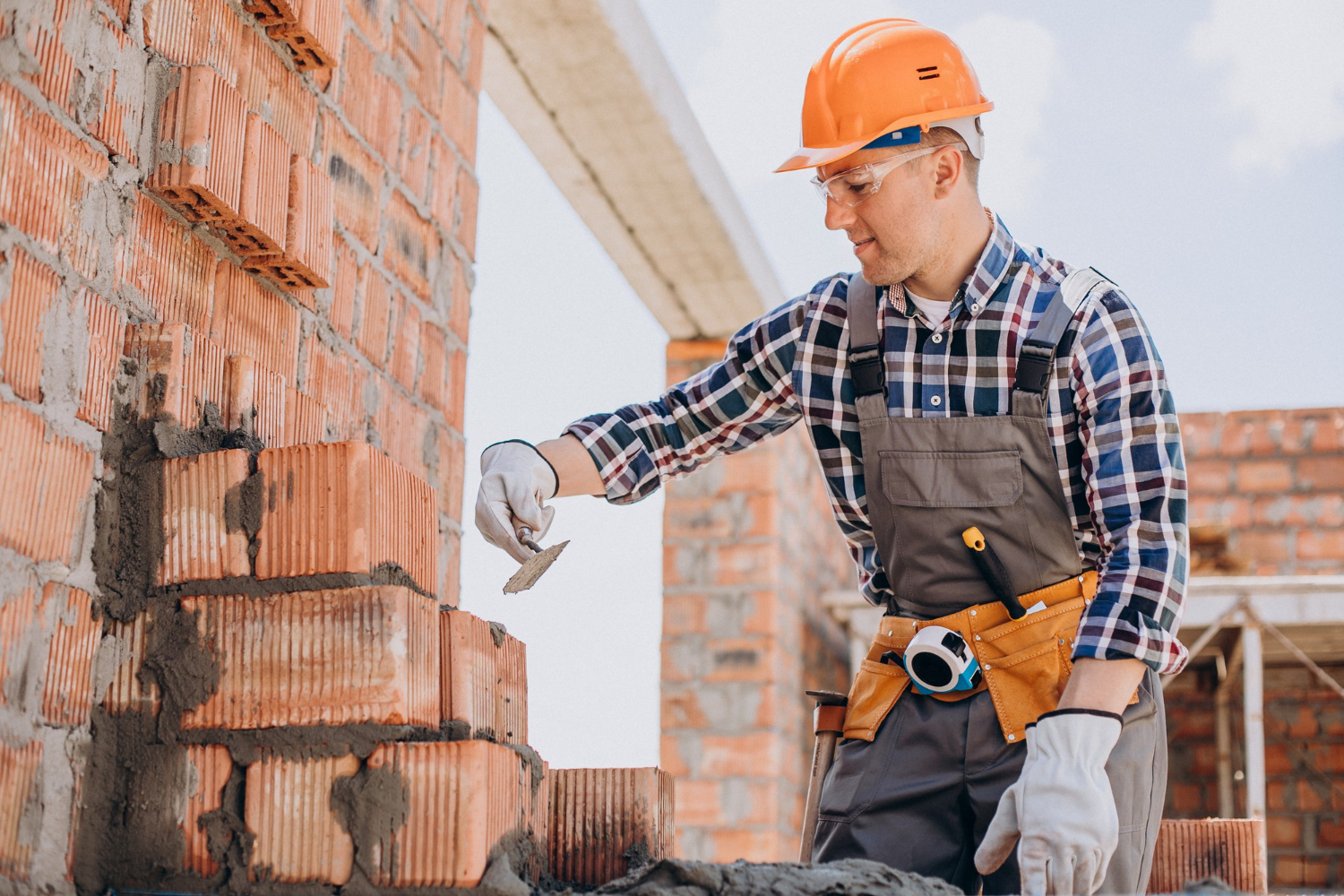 Un maçon monte un mur de briques et réalise les joints en béton à la truelle